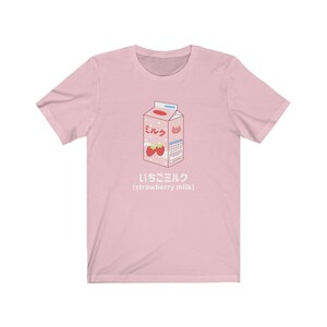 May include: Pink t-shirt with a cartoon illustration of a carton of strawberry milk. The carton is labeled "ミルク" (milk) and "いちごミルク" (strawberry milk).