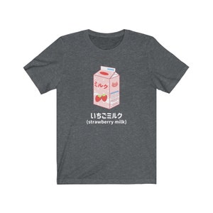 May include: A dark heather grey t-shirt with a cartoon illustration of a pink carton of strawberry milk. The carton has the Japanese word "ミルク" (milk) and the text "いちごミルク (strawberry milk)".
