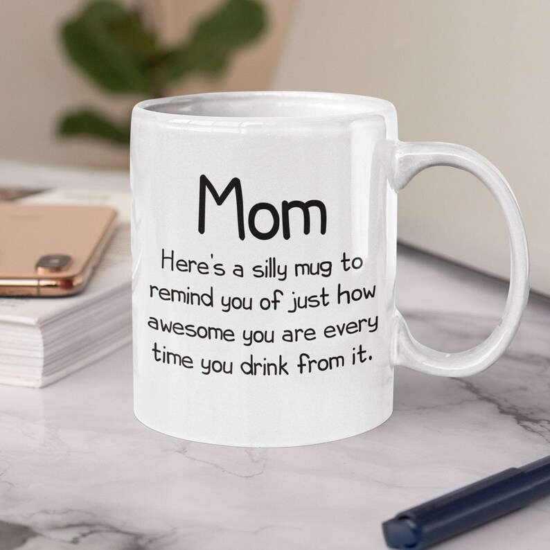 May include: White ceramic coffee mug with black text that reads "Mom Here's a silly mug to remind you of just how awesome you are every time you drink from it."