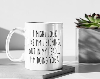 Può includere: Una tazza in ceramica bianca con testo nero che dice "IT MIGHT LOOK LIKE I'M LISTENING, BUT IN MY HEAD... I'M DOING YOGA"
