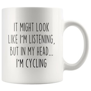 May include: White ceramic coffee mug with black text that reads "It might look like I'm listening, but in my head... I'm cycling."
