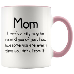 May include: White ceramic coffee mug with a pink rim and handle. The mug has black text that reads "Mom Here's a silly mug to remind you of just how awesome you are every time you drink from it."