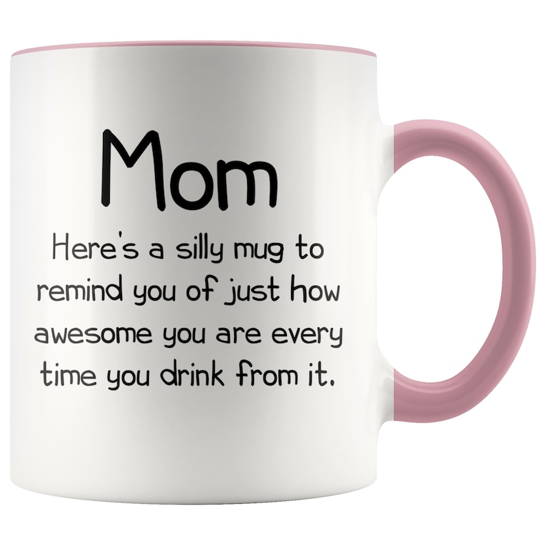 May include: White ceramic coffee mug with a pink rim and handle. The mug has black text that reads "Mom Here's a silly mug to remind you of just how awesome you are every time you drink from it."