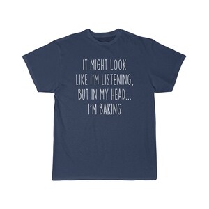 K&ouml;nnte beinhalten: Ein marineblaues T-Shirt mit wei&szlig;em Text, der "It might look like I'm listening, but in my head... I'm baking." lautet.
