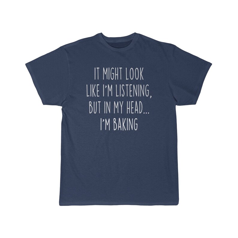 K&ouml;nnte beinhalten: Ein marineblaues T-Shirt mit wei&szlig;em Text, der "It might look like I'm listening, but in my head... I'm baking." lautet.