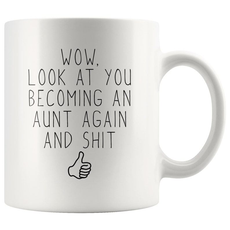 May include: White ceramic coffee mug with black text that reads "WOW, LOOK AT YOU BECOMING AN AUNT AGAIN AND SHIT" with a thumbs up emoji.