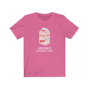 May include: Pink t-shirt with a cartoon illustration of a carton of strawberry milk. The carton is labeled "ミルク" (milk) and "いちごミルク" (strawberry milk).