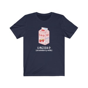 May include: A navy blue t-shirt with a cartoon illustration of a pink carton of strawberry milk. The carton has the Japanese word "ミルク" (milk) and the text "いちごミルク (strawberry milk)".