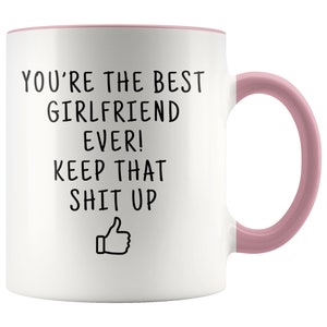 May include: White ceramic coffee mug with a pink rim and handle. The mug has black text that reads "You're the best girlfriend ever! Keep that shit up" with a thumbs up emoji.