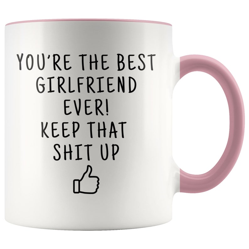 May include: White ceramic coffee mug with a pink rim and handle. The mug has black text that reads "You're the best girlfriend ever! Keep that shit up" with a thumbs up emoji.