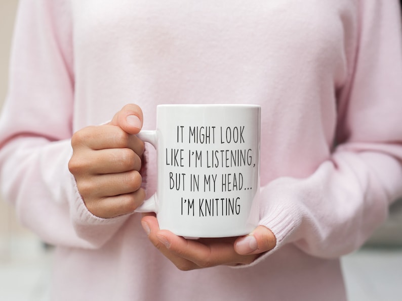 May include: White ceramic mug with black text that reads "It might look like I'm listening, but in my head... I'm knitting".