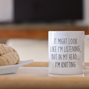May include: White ceramic mug with black text that reads "It might look like I'm listening, but in my head... I'm knitting".