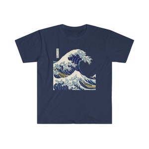 May include: A navy blue t-shirt with a graphic print of a large blue wave crashing over a boat. The wave is depicted in a traditional Japanese style, with white foam and a dark blue background. The text "神奈川沖浪裏" is printed in black on the left side of the wave.