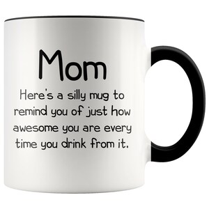 May include: White ceramic coffee mug with a black rim and handle. The mug has black text that reads "Mom Here's a silly mug to remind you of just how awesome you are every time you drink from it."