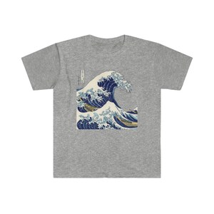 May include: A grey t-shirt with a graphic print of a blue and white wave. The wave is a famous Japanese artwork called "The Great Wave off Kanagawa".