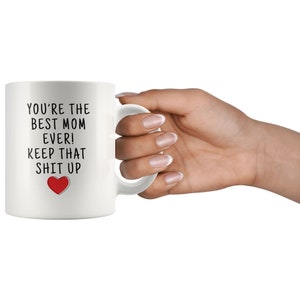 May include: White ceramic coffee mug with black text that reads "You're the best mom ever! Keep that shit up" and a red heart.