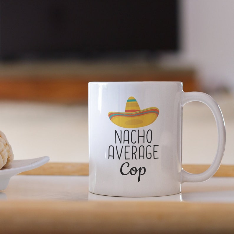 May include: White ceramic mug with a black and white graphic of a sombrero and the text "Nacho Average Cop".