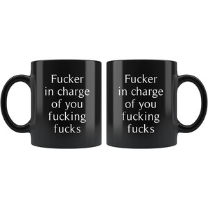 May include: Two black ceramic mugs with white text that reads "Fucker in charge of you fucking fucks". The mugs are identical and have a standard handle.