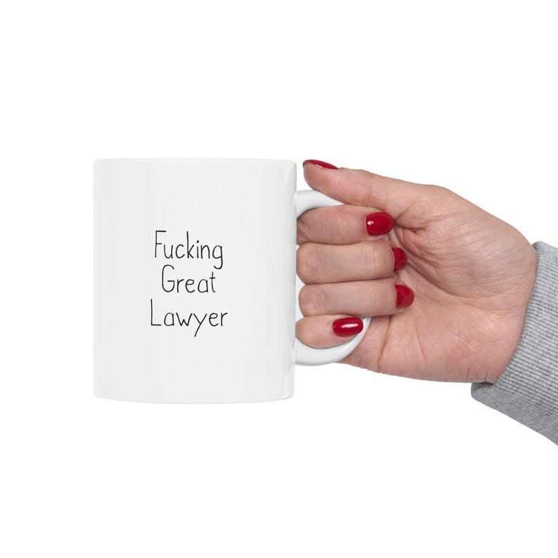 Może przedstawiać: Biały kubek ceramiczny z napisem "Fucking Great Lawyer" napisanym czarnym markerem.