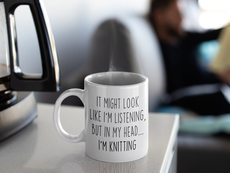 May include: White ceramic coffee mug with black text that reads "It might look like I'm listening, but in my head... I'm knitting".