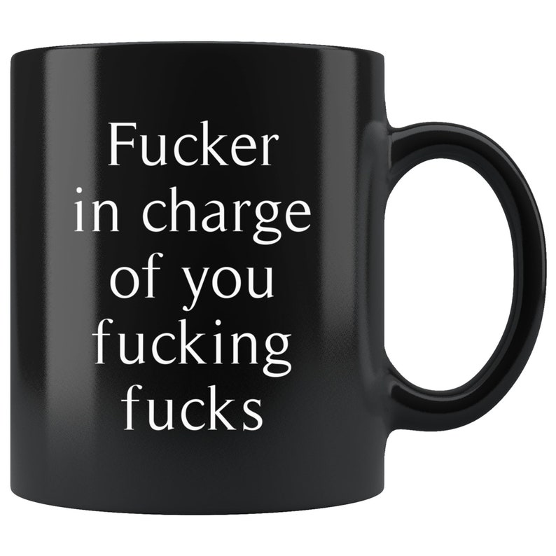 May include: Black ceramic coffee mug with the text "Fucker in charge of you fucking fucks" in white, a humorous and bold statement. The mug has a standard handle and a glossy finish.