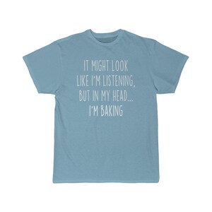 K&ouml;nnte beinhalten: Ein hellblaues T-Shirt mit dem Text "It might look like I'm listening, but in my head... I'm baking" in wei&szlig; gedruckt.