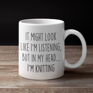 May include: White ceramic mug with black text that reads "It might look like I'm listening, but in my head... I'm knitting".