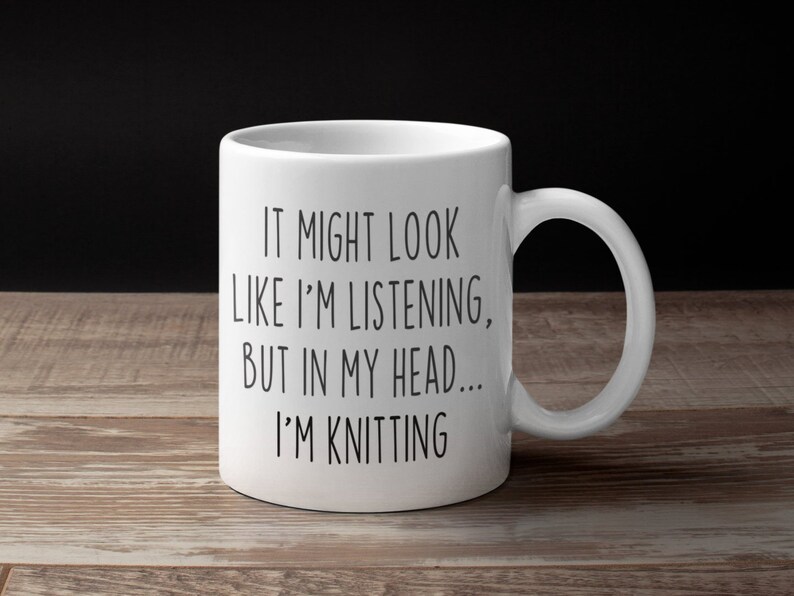 May include: White ceramic mug with black text that reads "It might look like I'm listening, but in my head... I'm knitting".