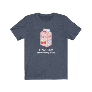 May include: A navy blue t-shirt with a cartoon illustration of a pink carton of strawberry milk. The carton has Japanese text that says "Milk" and "Strawberry Milk".