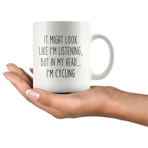 May include: White ceramic coffee mug with black text that reads "It might look like I'm listening, but in my head... I'm cycling."