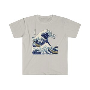May include: A light grey t-shirt with a blue and white graphic print of a large wave crashing. The graphic is a reproduction of the famous Japanese woodblock print "The Great Wave off Kanagawa" by Katsushika Hokusai.