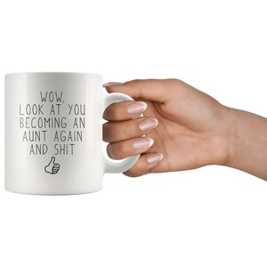 May include: White ceramic mug with black text that reads "WOW. LOOK AT YOU BECOMING AN AUNT AGAIN AND SHIT" with a thumbs up emoji.