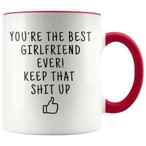 May include: White ceramic coffee mug with a red rim and handle. The mug has black text that reads "You're the best girlfriend ever! Keep that shit up" with a thumbs up emoji.