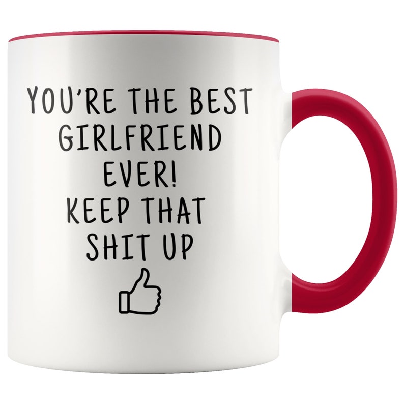 May include: White ceramic coffee mug with a red rim and handle. The mug has black text that reads "You're the best girlfriend ever! Keep that shit up" with a thumbs up emoji.