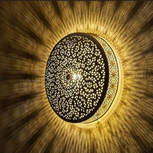 Op de afbeelding: Een ronde, decoratieve plafondlamp met een ingewikkeld, geometrisch patroon. De lamp is gemaakt van licht materiaal en geeft een warm licht.