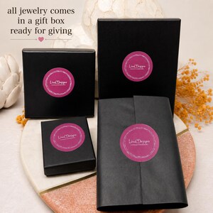 Four black gift boxes and a wrapped package, each with a pink circular sticker that reads "Lisa Designs". The text "all jewelry comes in a gift box ready for giving" is at the top of the image.