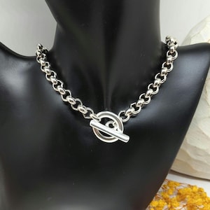 May include: A silver chain necklace with a toggle clasp, displayed on a black mannequin. The chain is made of round, connected links. The toggle clasp features a bar that slots through a circular loop.