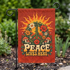 May include: A rectangular garden flag with a red background featuring a central peace sign formed by green vines, white and orange daisies, and red mushrooms. Above is a yellow sun, and below is the text PEACE LIVES HERE in yellow letters.
