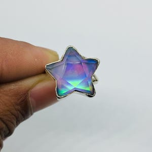 Puede incluir: Un anillo de plata con una gran piedra preciosa en forma de estrella iridiscente. La piedra es de color morado oscuro con toques de azul y verde.