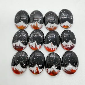May include: Twelve oval-shaped black cabochons with white and red mountain scenes. The cabochons have a speckled black background with white and red details.
