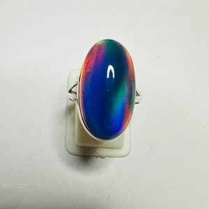 May include: A silver ring with a large oval-shaped iridescent gemstone. The gemstone is a deep blue color with hints of pink, green, and purple.