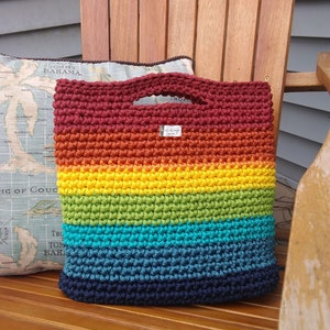 Pu&ograve; includere: Una borsa a mano all'uncinetto con un motivo arcobaleno. La borsa &egrave; realizzata con una variet&agrave; di colori, tra cui rosso, arancione, giallo, verde, blu e viola. La borsa ha un'unica maniglia e un piccolo cartellino che dice "Fatto a mano".