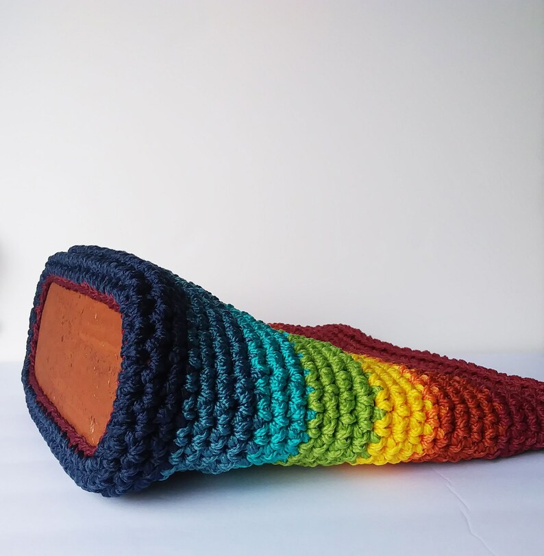 Pu&ograve; includere: Una borsa a mano in crochet arcobaleno con uno schema di colori blu scuro, verde acqua, verde, giallo, arancione e rosso. La borsa &egrave; realizzata con un filato spesso e testurizzato.