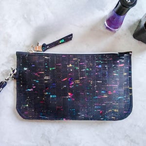 May include: A black cork clutch with a colorful confetti pattern and a detachable strap. The clutch has a zipper closure.