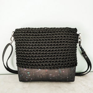 May include: A black crocheted crossbody bag with a cork bottom. The bag has a black strap and silver hardware.
