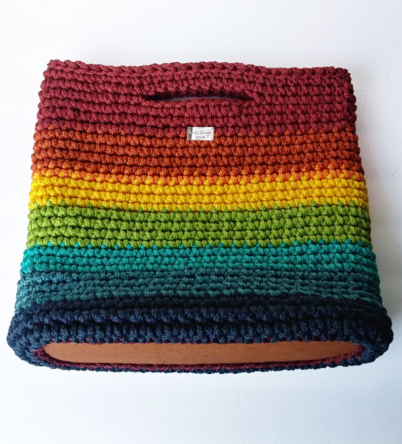 Pu&ograve; includere: Una borsa a mano in crochet arcobaleno con una base in legno. La borsa &egrave; realizzata con una variet&agrave; di colori, tra cui rosso, arancione, giallo, verde, blu e viola.
