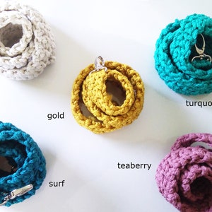 May include: A collection of crocheted straps in various colors, including ivory, gold, turquoise, surf, and teaberry. Each strap is coiled and features a silver-tone clasp or ring. The text labels each color.