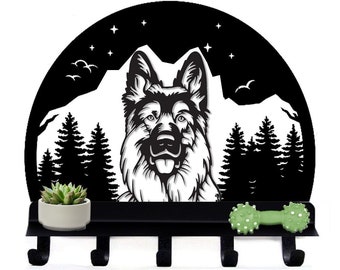 Puede incluir: Porta llaves de metal negro con una silueta de un pastor alemán frente a una cordillera y pinos. El porta llaves tiene cinco ganchos y una pequeña planta suculenta en maceta. Un juguete para perros de goma verde está a la derecha del porta llaves.