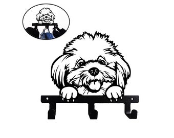 May include: Black metal key holder shaped like a dog with a white fluffy coat. The dog is looking up with its tongue sticking out. There are three hooks on the holder.