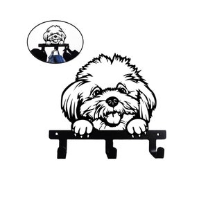 May include: Black metal key holder shaped like a dog with a white fluffy coat. The dog is looking up with its tongue sticking out. There are three hooks on the holder.